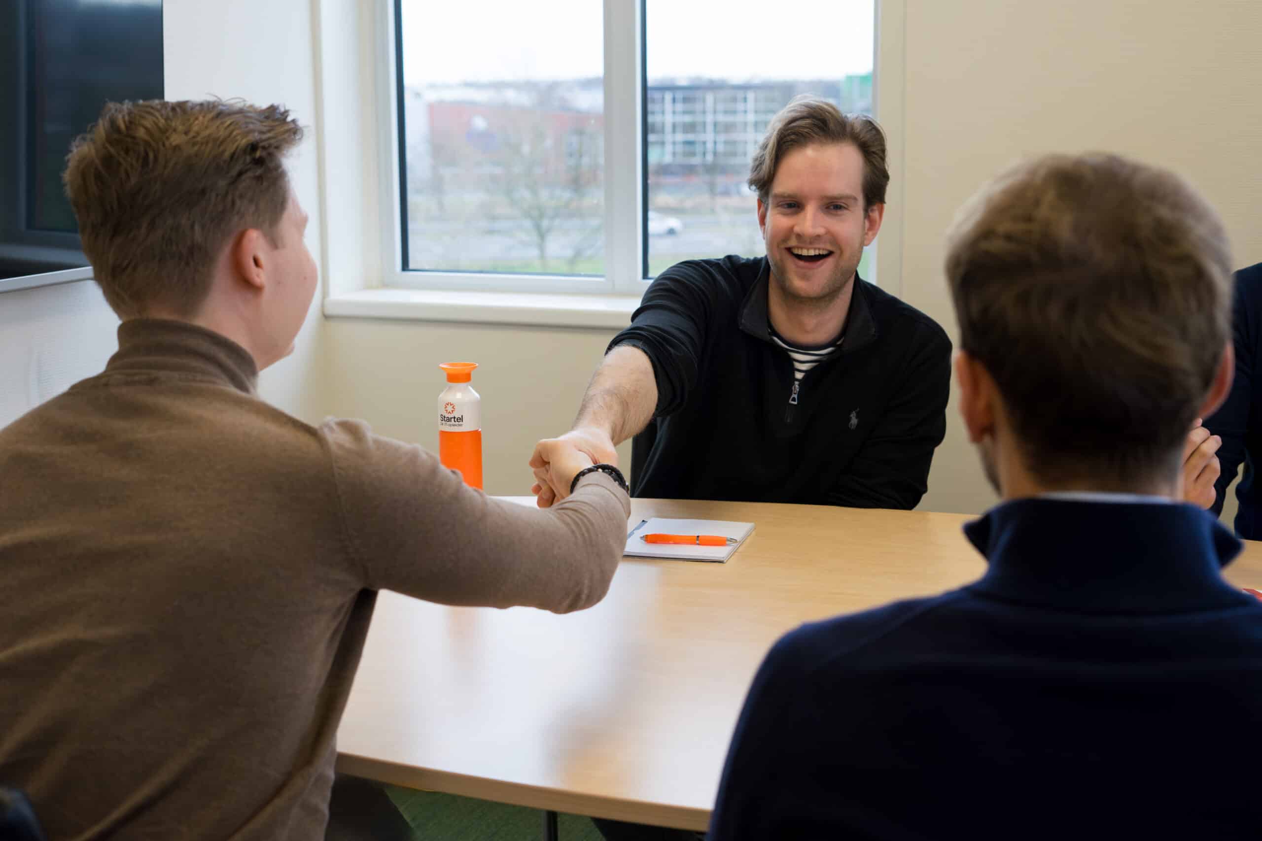 Twee medewerkers van Startel geven elkaar een hand aan tafel.