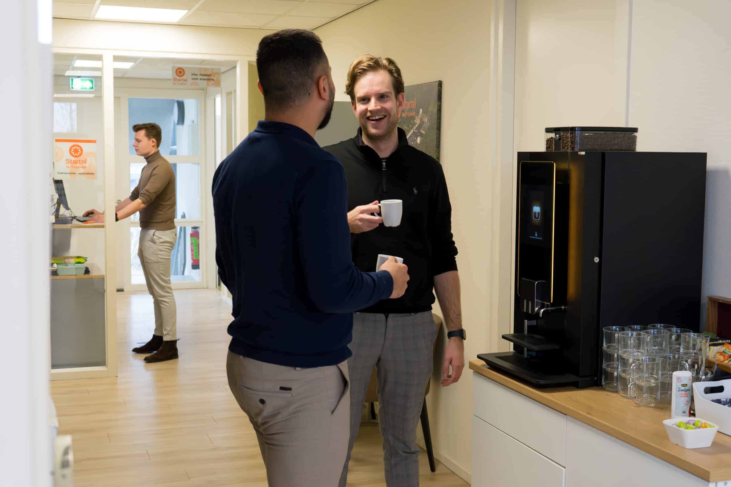 Twee medewerkers van Startel staan bij de koffieautomaat.